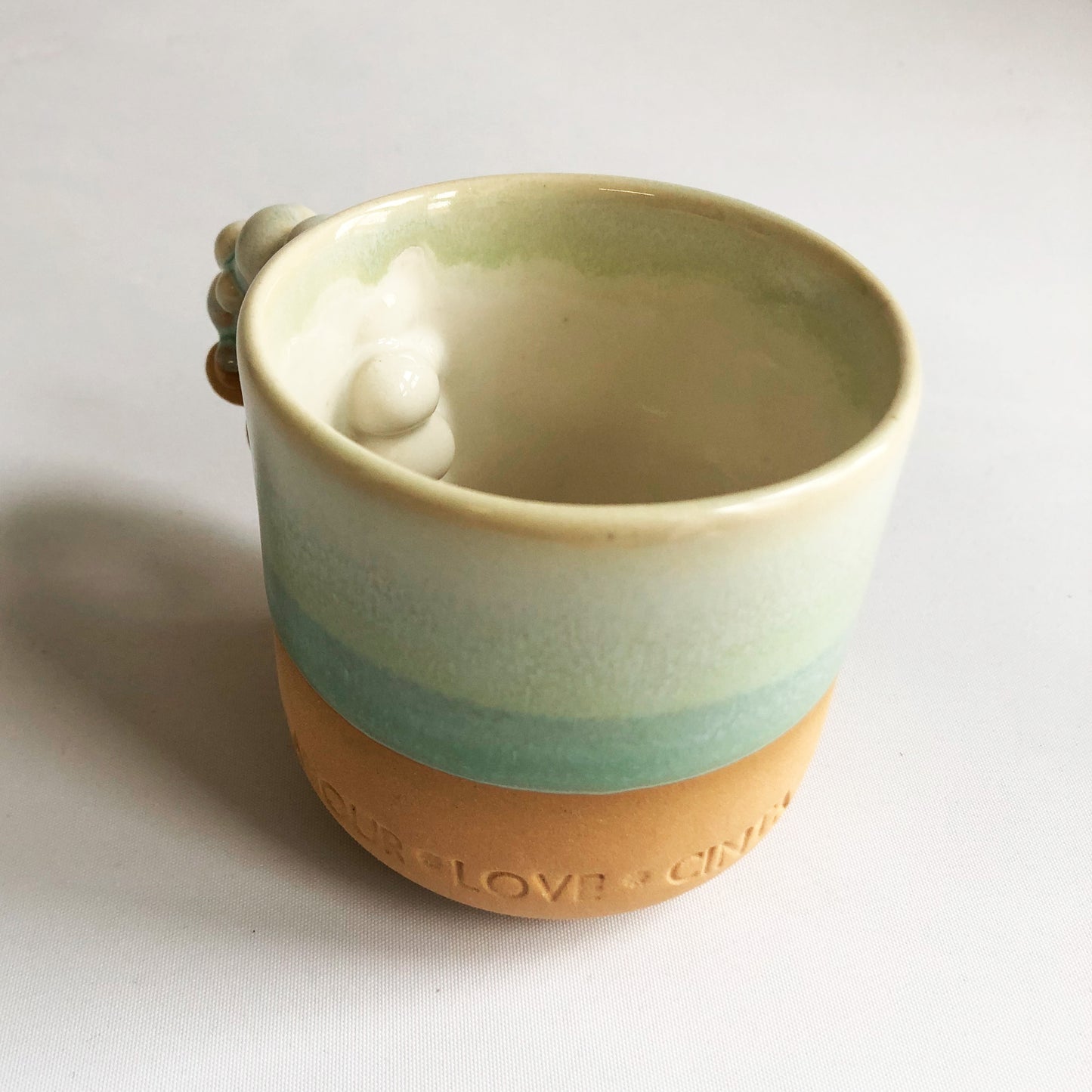 Little cup with text. The cup has a matte ocher colored bottom and green glaze