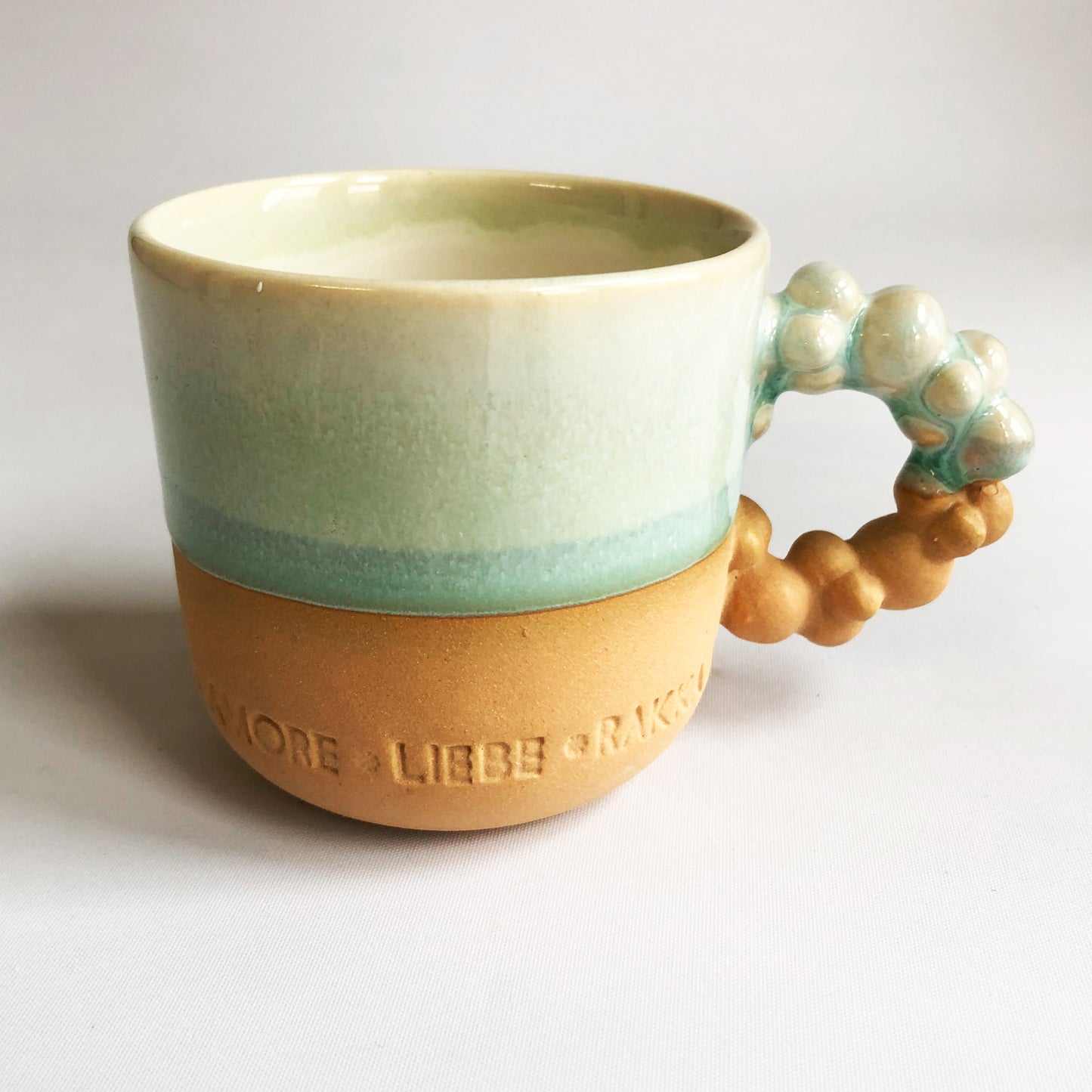 Little cup with text. The cup has a matte ocher colored bottom and green glaze