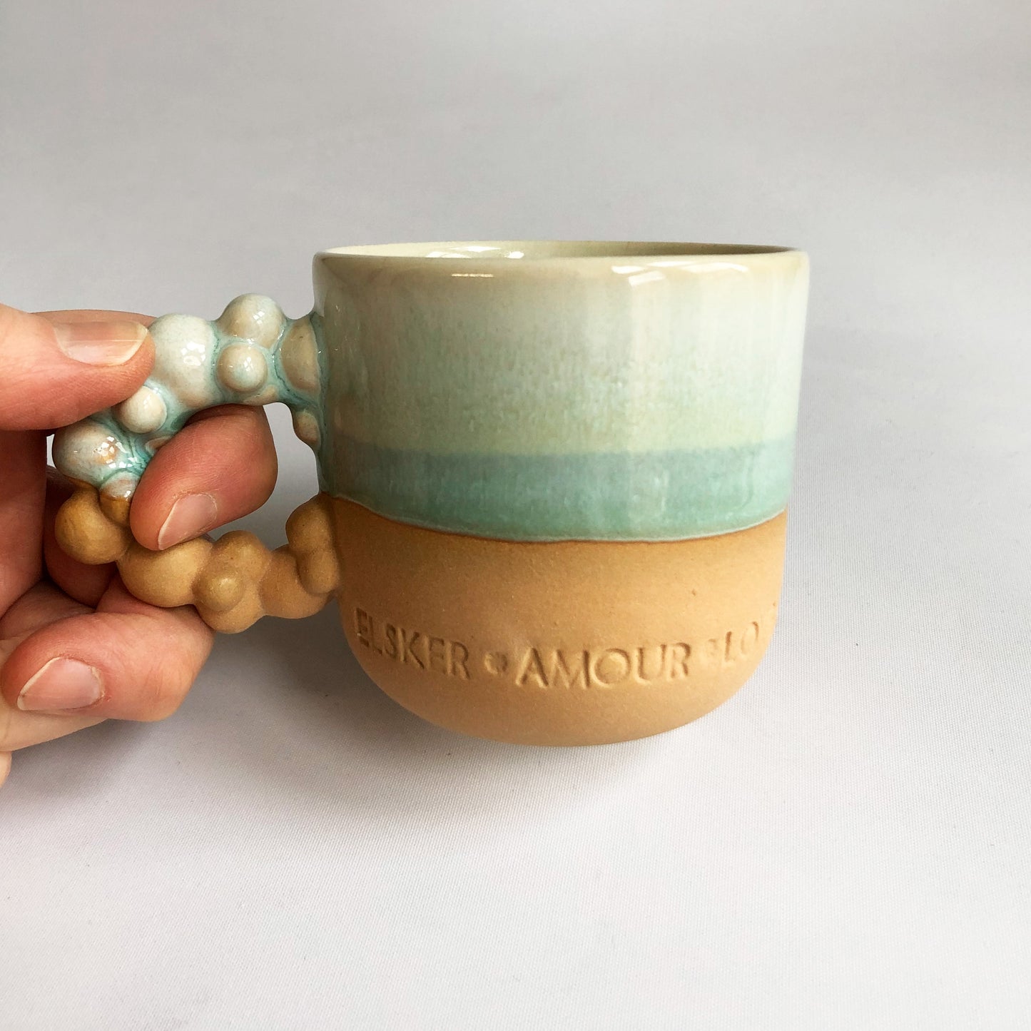 Little cup with text. The cup has a matte ocher colored bottom and green glaze