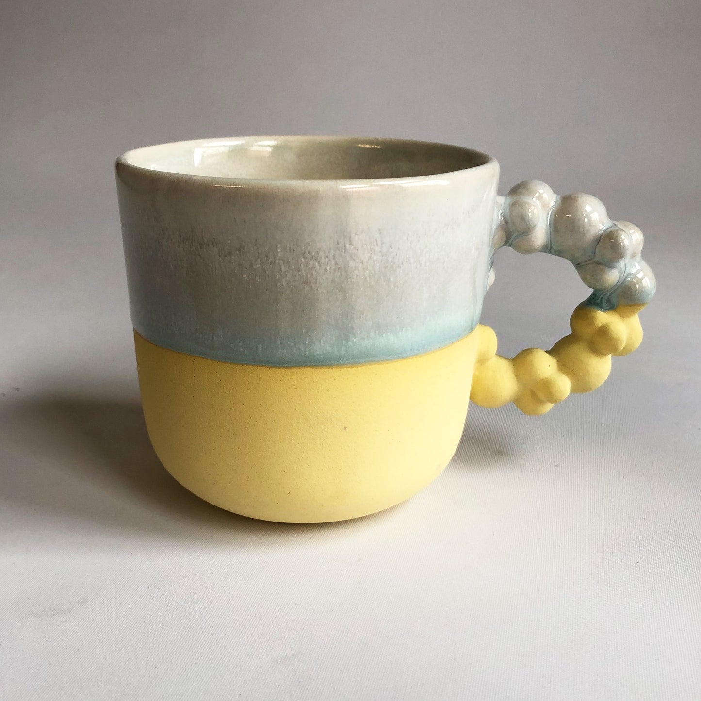 Big cup with text. The cup has a matte yellow bottom and a iceblue glaze