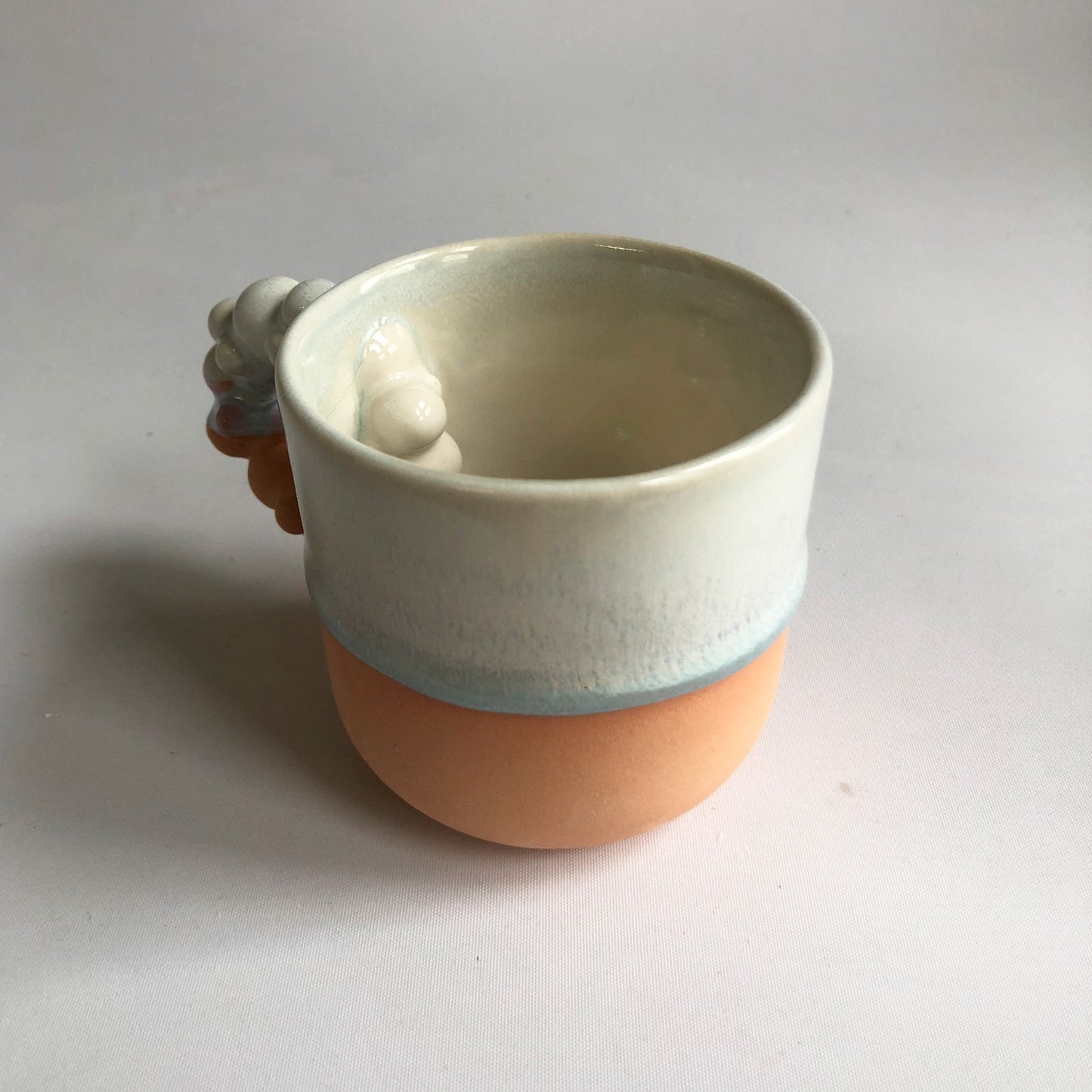 Little cup with matte peach colored bottom and iceblue glaze