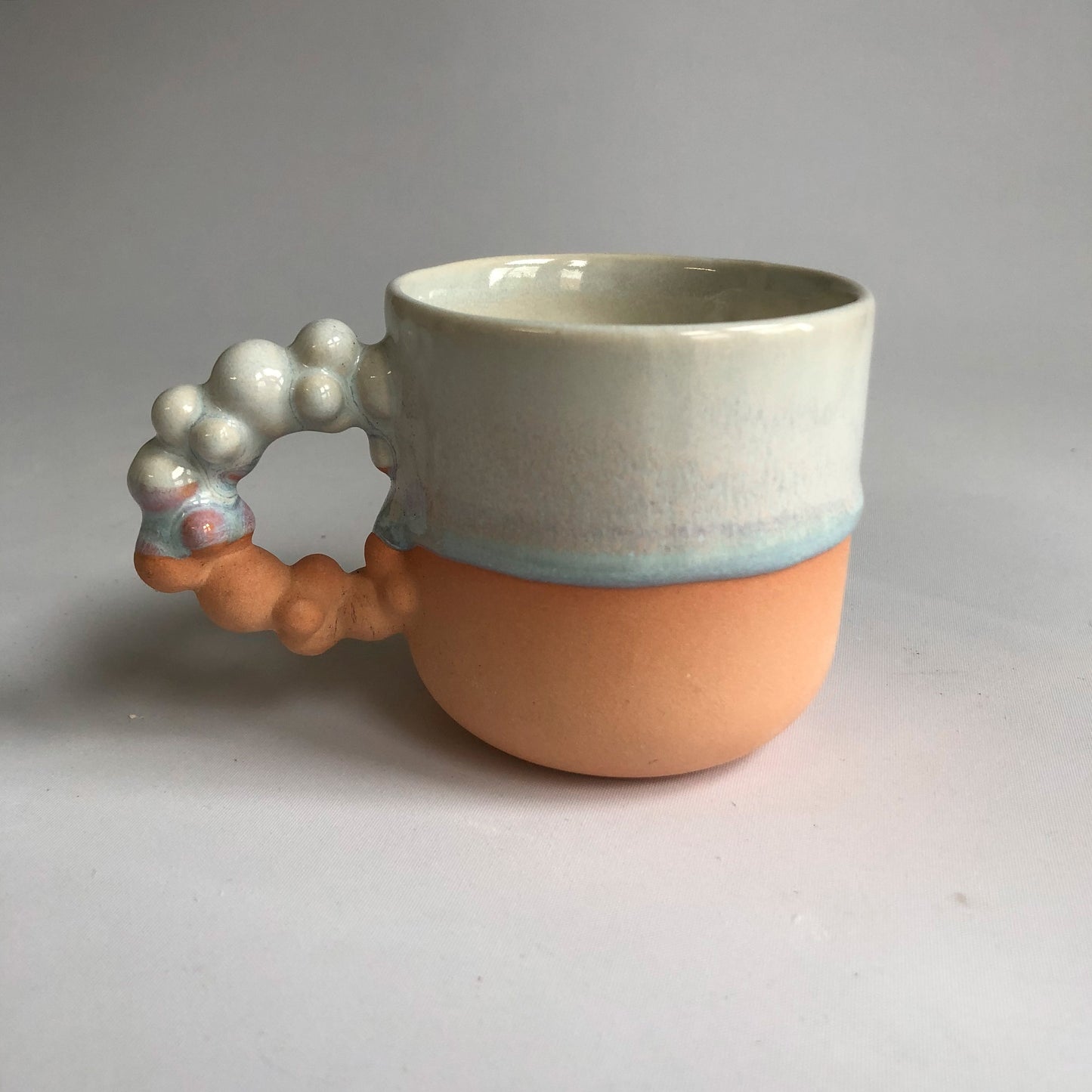 Little cup with matte peach colored bottom and iceblue glaze