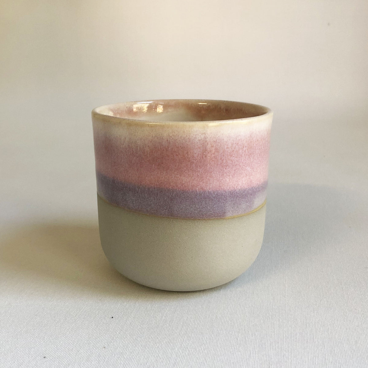 Large handleless cup with a matte grey bottom and light pink glaze